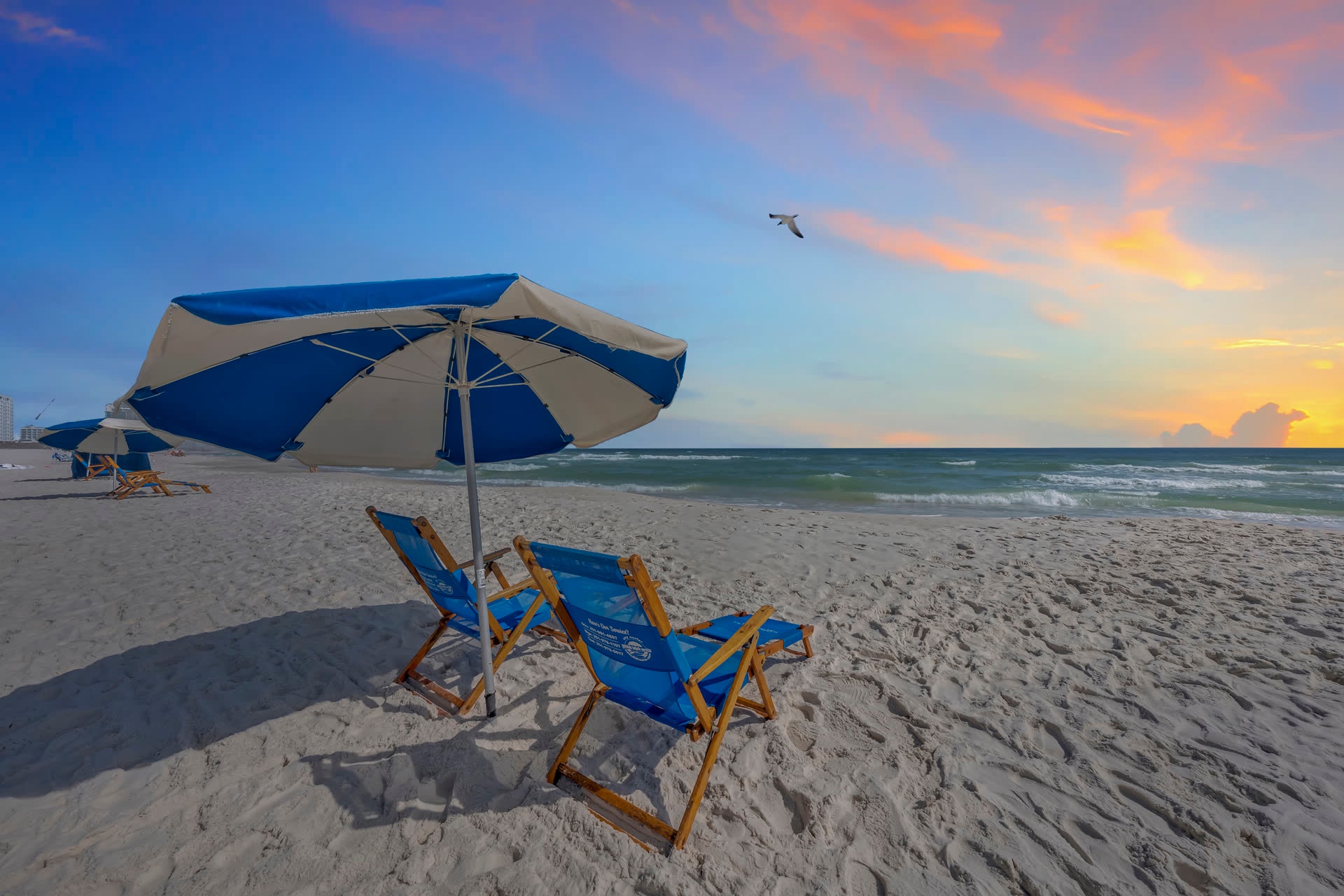 Beach chairs and an umbrella on the sand at sunset