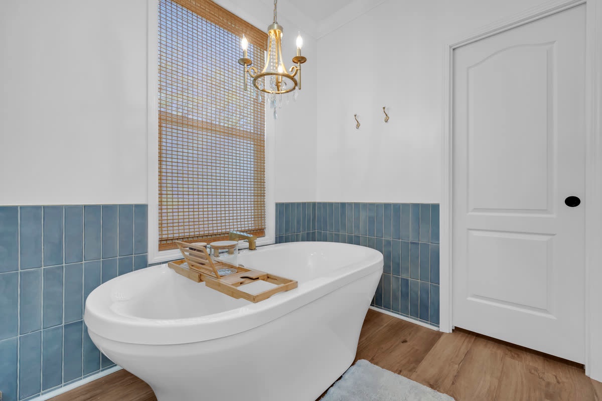 Freestanding soaking tub with a tiled accent wall and chandelier