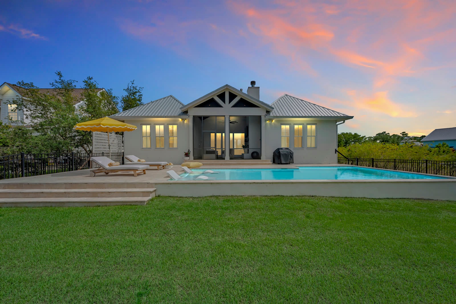 Coastal home exterior at twilight with a glowing pool and sunset sky