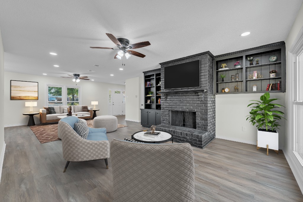 Virtually staged great room with grey brick fireplace, blue accent chairs, and built-in shelving