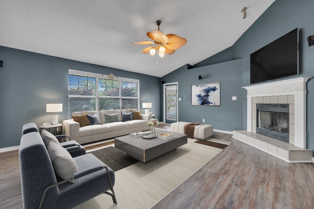 Virtually staged living room with vaulted ceiling, blue accent chairs, and fireplace with mounted TV
