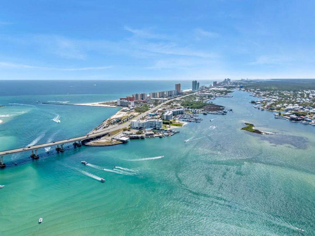 Aerial view of a coastal city and bay with turquoise water, boats, marina, and high-rise buildings along the shoreline